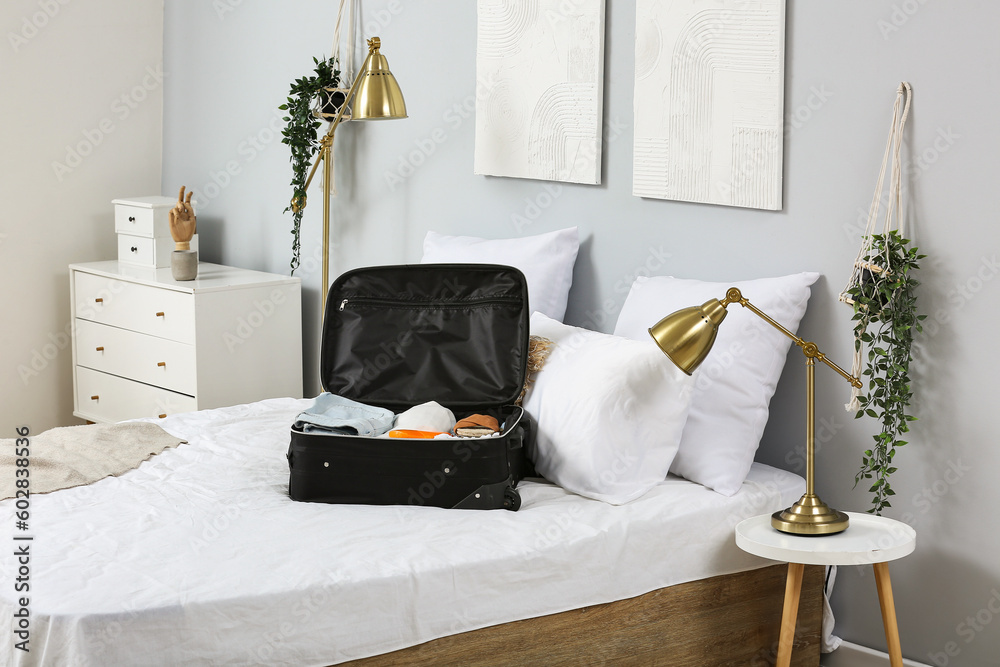 Open suitcase with female clothes on bed in room