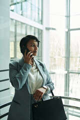 Poster - Young confident female agent in formalwear standing in elevator and talking to client on smartphone while hurrying for conference