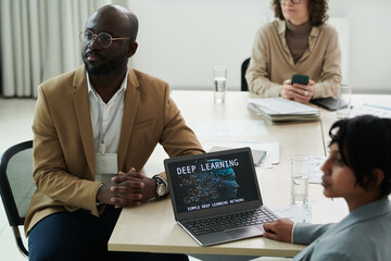 Poster - Young serious businessman and his colleagues listening to report of speaker while sitting by desk during lecture about deep learning
