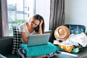 Stressed Asian woman worried about online booking errors or making the wrong travel plans on her summer vacation. Sadness girl fell down due to the trip has been cancelled. Travel and holiday concept.