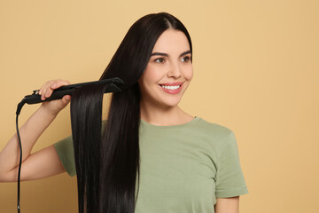 Poster - Beautiful happy woman using hair iron on beige background