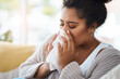 Sick, cold and a woman blowing nose on sofa with covid, virus or allergies in a house. Flu, healthy and a young lady with an allergy, sinus problem or sneezing into a tissue on the living room couch