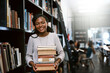 © Jadon B/peopleimages.com - Portrait, education and black woman with books, library and university with a smile, bookshelf and studying. Face, female person or happy student with research, literature and learning with knowledge