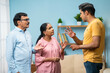 angry Indian adult son arguing with elderly senior parents at home - concept of irresponsibility, family problems and generation gap
