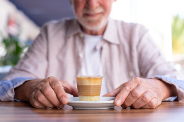 Wall Mural - Senior man sitting outdoors at a cafe table enjoying coffee with milk - Caucasian senior grandfather relaxing in coffee break