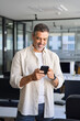 Vertical portrait of middle aged Latin or Indian business man using phone mobile technology application for online work communication. Smiling mature Hispanic businessman holding smartphone in office.