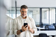 © Stock 4 You - Smiling mature Latin or Indian businessman holding smartphone in office. Middle aged manager using cell phone mobile app. Digital technology application and solutions for business success development.