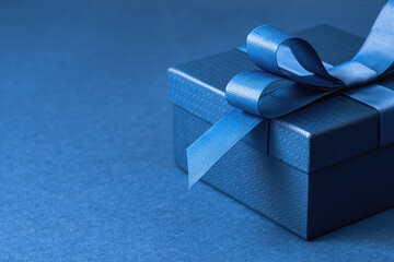 Luxury gift box with a blue bow on blue. High angle view monochrome close up. Fathers day or Valentines day gift for him. Corporate gift concept or birthday party. Festive sale