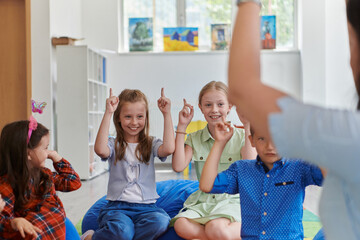 Wall Mural - A happy female teacher sitting and playing hand games with a group of little schoolchildren