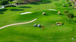 © Bulat - Top view of two men playing golf on a sunny summer day. Aerial view of the green golf course. Hitting the ball with a golf stick. An active type of recreation. Golf car