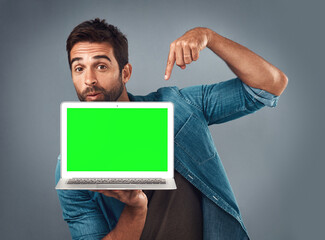 Poster - Man, laptop and pointing on mockup green screen for advertising or marketing against a grey studio background. Portrait of male person showing computer display, chromakey or mock up for advertisement