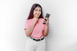 A thoughtful young woman wearing pink t-shirt, holding her chin and her phone isolated by white background