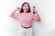 © Reezky - A young Asian woman with a happy successful expression wearing pink t-shirt and holding smartphone isolated by white background