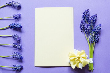 Poster - Bouquet of blue grape mouse hyacinths and gift box with ribbon over purple paper background. Blank greeting card mockup. Minimal floral frame made of flowers. Flat lay, top view. Lovers or Women's day