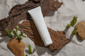 Sticker - An empty white plastic tube placed on brown logs on sand background with small cactus and rock. Mockup scene for cosmetics product, lotion or cleanser. Natural desert concept