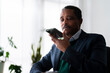 © Studio Marmellata - adult Ethiopian male CEO director in formal suit making conversation on mobile phone recording voice message while working in office