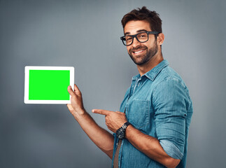 Poster - Happy man, tablet and pointing to green screen for advertising against a grey studio background. Portrait of male person showing technology display, chromakey or mockup for copy space advertisement