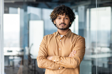 Portrait of a successful young hispanic programmer standing in a modern office with his arms crossed on his chest and looking confidently at the camera
