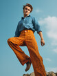 A man in bight orange bell pants blue porka dot shirt  in the style of neo pop sensibility, clear blue sky background, generative ai