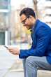 © mimagephotos - Smiling african businessman sitting outside using cell phone