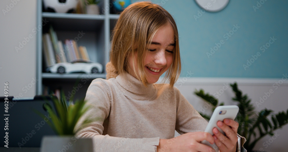 Smiling cute preteen girl use mobile phone sitting by table in living ...