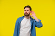 © kinomaster - Young, serious, blond man in a blue shirt on a yellow background, holding an ear to listen better, what you're saying. Photo Shoot.