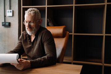 Wall Mural - Handsome mature grey haired man reading paper documents in office