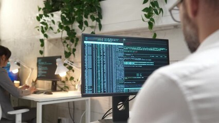 Rear view on busy male programmer coding and programming software on computer. On PC monitor visible big data. Man working on program codes in modern office. Creating websites for customer.