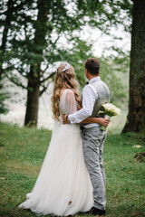 The bride and groom stand after wedding ceremony. A newlywed couple hugging in a country in their honeymoon. photo on nature, forest, outdoors.