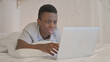Young African Man Shocked by Loss on Laptop while Lying on Stomach in Bed