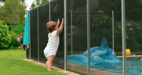 Wall Mural - Baby leaning on swimming pool fence protection. Infant standing on safety gate