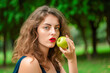 © jovannig - A young woman eating an apple outdoor in the park - Generative AI