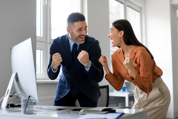 Excited colleagues gesturing YES, celebrating business success in front of computer in office, copy space