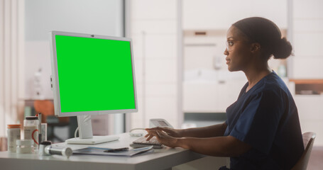 Wall Mural - Portrait of a Black Female Medical Health Care Professional Working on Desktop Computer with Green Screen Mock Up Display in Hospital Office. Clinic Head Nurse is Appointing Prescriptions Online