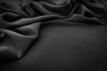 Texture of satin or silk fabric in black color. Textile. Fabric background with folds and waves