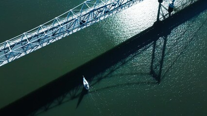 Wall Mural - Sailing boat and bridge. Aerial view of the bridge of Helrcilio Luz in the city of Florianopolis during sunny day with sailing boat sailing under it in the sea. Brazil