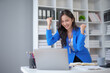 © amnaj - Happy asian businesswoman raising hands with victory smiling happily with laptop computer. The concept of success at work.