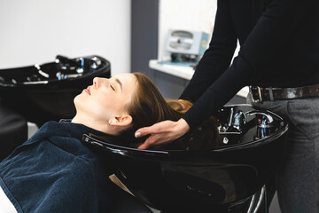 Poster - Master woman hairdresser gently washes the girl's hair with shampoo and conditioner before styling in a beauty salon.