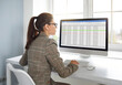 Female accountant working with corporate financial data on computer. Young woman in suit sitting at office desk and looking at business spreadsheets on screen of modern desktop computer
