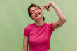 © Viktor Solomin/Stocksy - Happy young woman showing V gesture on green background