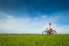 Happy Young Woman On A Green Meadow Riding A Bicycle