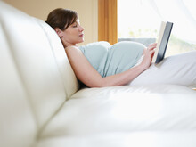 Italian 7 Months Pregnant Woman Lying Down On Sofa And Reading Book. Horizontal Shape, Side View, Copy Space