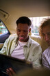 © Jovo Jovanovic/Stocksy - Two men using digital tablet while traveling in backseat of car