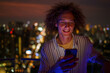© Jovo Jovanovic/Stocksy - Smiling man using mobile phone on rooftop at night