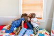 © ByLorena/Stocksy - Grandma with grandchildren big hugs in bedroom