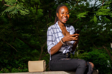 beautiful young african lady smiling while using her phone outdoors