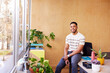 © ALTO IMAGES/Stocksy - Smiling black man sitting in office with big windows and plants
