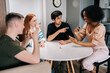 © dikushin - Cheerful multiethnic friends having play cards games for time enjoying board games activity for entertainment at home. Cheerful diverse men and women playing UNO board game sitting at table.