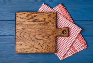 Wall Mural - Cutting board over kitchen towel on blue kitchen table background. Recipe. Kitchenware. Empty modern wooden cutting board. Menu. MOCKUP. Place for text. Place to copy.