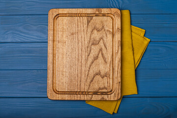 Wall Mural - Cutting board over kitchen towel on blue kitchen table background. Recipe. Kitchenware. Empty modern wooden cutting board. Menu. MOCKUP. Place for text. Place to copy.